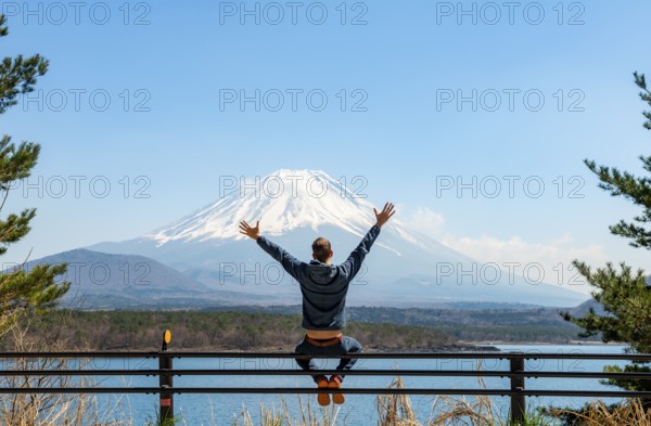 Young man sitting on railings next to a road and stretching his arms in the air, looking across the