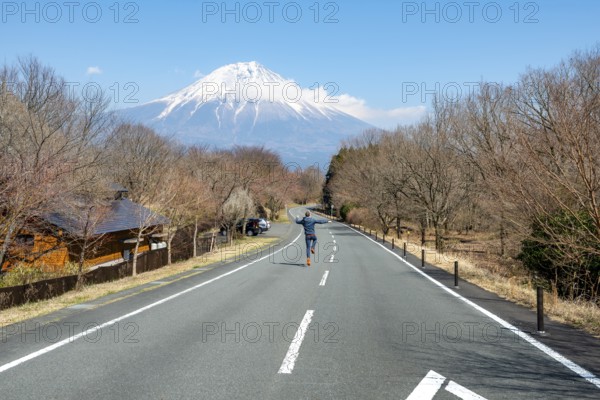 Young man jumping on road, road leading to Mount Fuji volcano, wanderlust, Yamanashi Prefecture,