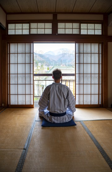 Young man wearing kimono sitting in traditional Japanese living room with tatami mats and shoji