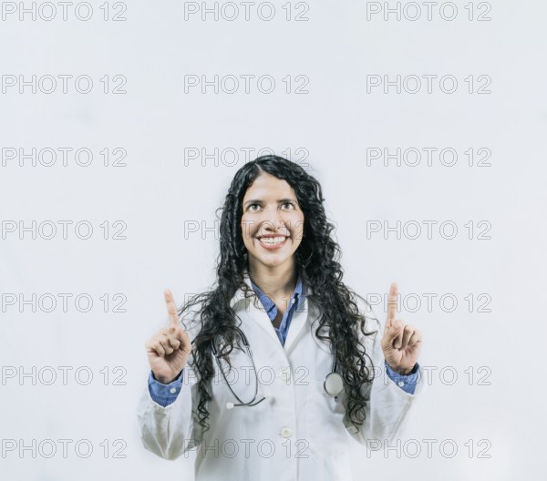 Cheerful female doctor pointing up isolated. Young female doctor looking and pointing at promotion