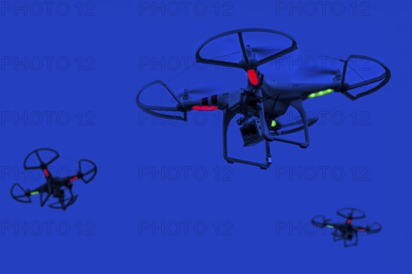 Three illuminated miniature quadcopter drones, teleoperated unmanned aerial vehicles, UAV equipped