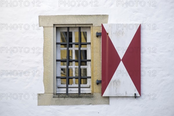 Window with red and white shutters and iron bars in front of a white wall, Münsterland, North