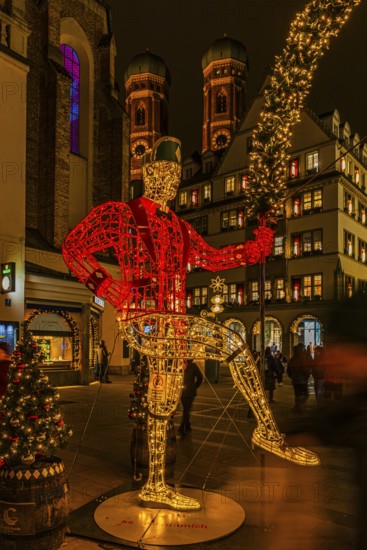 Schäffler dancers made of wire and string of lights, in the back the towers of the Church of Our