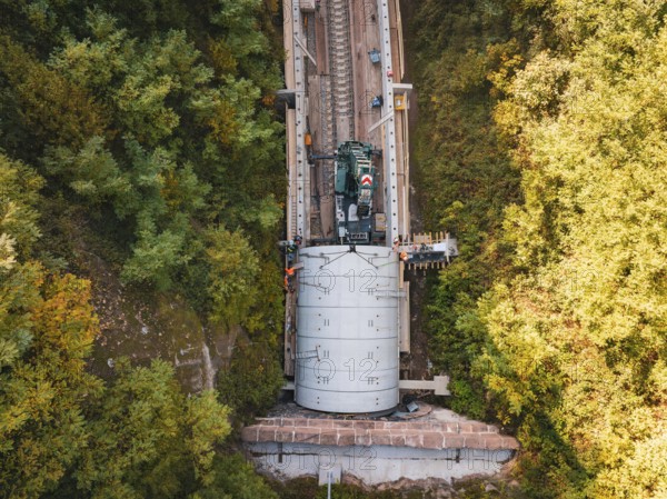 Crane photographed from the air above a tunnel opening in an autumnal landscape, building of