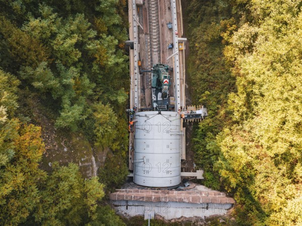 Bird's eye view shows crane over tunnel on a railway line surrounded by trees, construction of