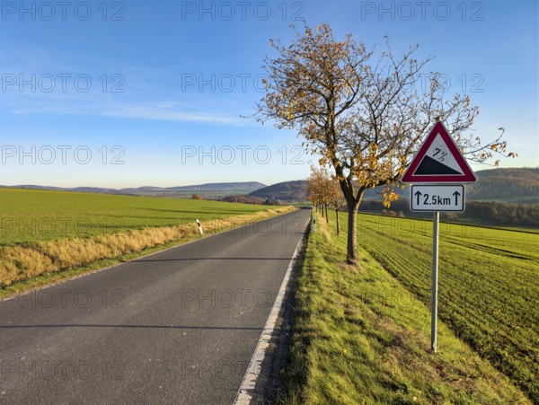 Country road through hilly, agricultural landscape, road sign warns of slopes, slopes, sunny autumn