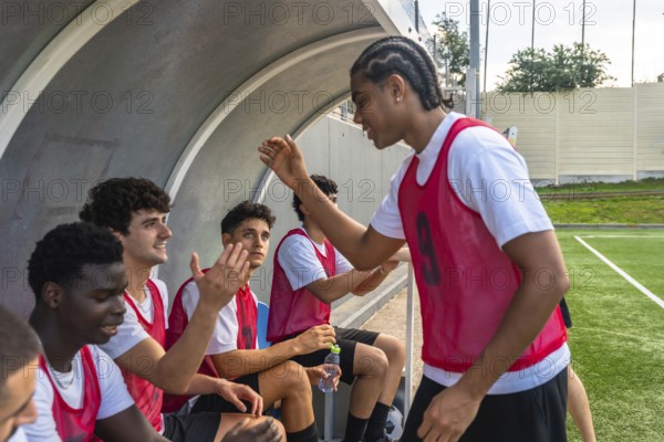 Soccer players in red bibs sitting on the bench and high fiving in the dugout, sharing a moment of