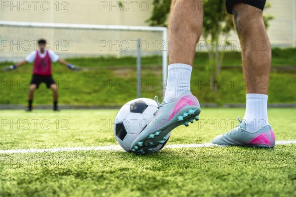 Soccer player's foot rests on a football, ready to take a penalty shot on a green artificial turf