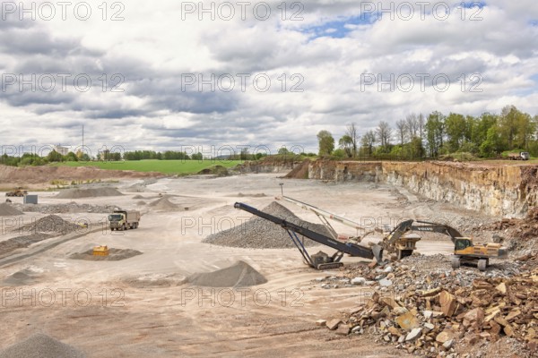 Excavator at a stone crusher with a conveyor in a limestone quarry with a waiting truck in a rural