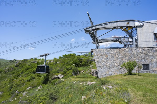 Cable car station with gondola in a green landscape, stone wall and bright blue sky, Tatev cable