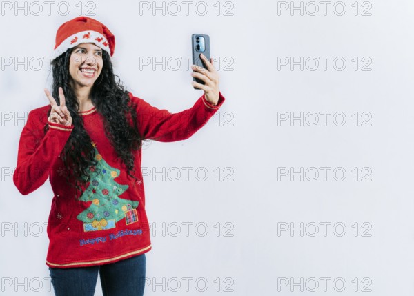 Happy young latin woman in Christmas sweater taking selfies isolated. Funny girl in Christmas hat