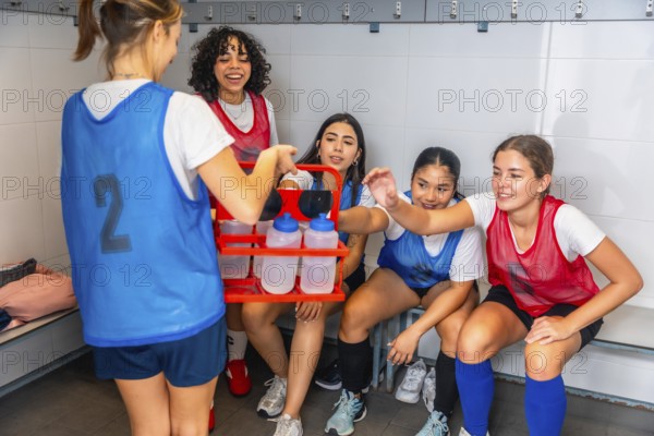 Teenagers from a diverse girls soccer team taking a water break and hydrating, showing friendship,