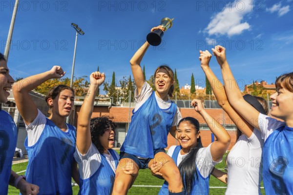 Female athletes sharing joy and success, lifting their teammate holding a trophy after winning a
