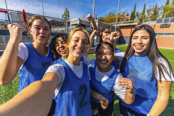 Group of smiling young women players celebrating success and victory on a soccer field, posing for