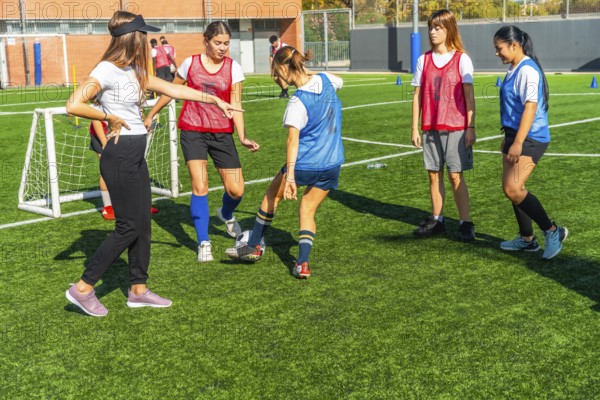 Female coach instructing a diverse group of young women soccer players on a green artificial turf