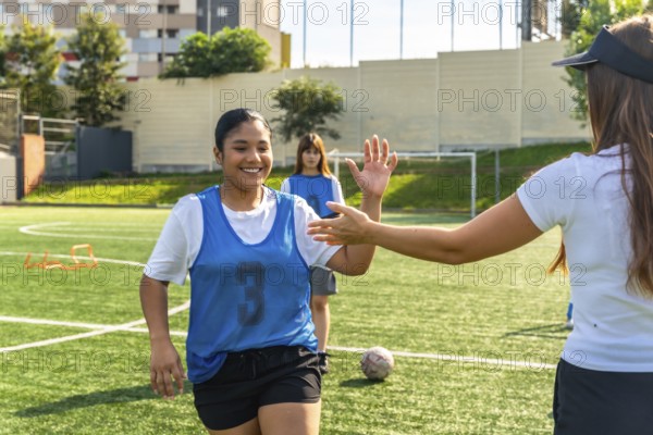 Young female soccer player smiling and high fiving her coach on a green field during practice,