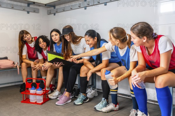 Diverse women's soccer team in uniforms sitting on benches in a locker room, gathered around their