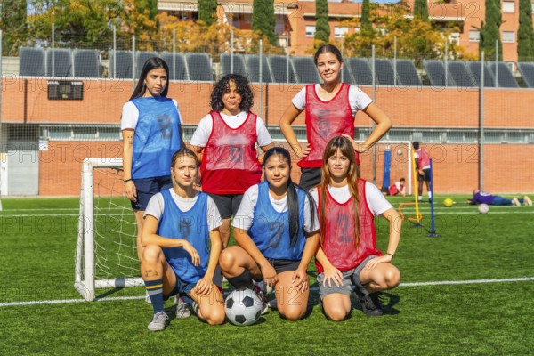 Diverse group of women on a soccer field, some standing and some crouching, wearing jerseys and