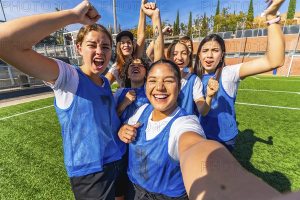 Group of excited multiracial women soccer players in blue vests and white t shirts celebrating