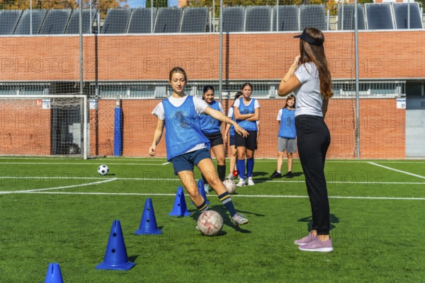 Group of diverse young women soccer players training with their coach on a green artificial turf