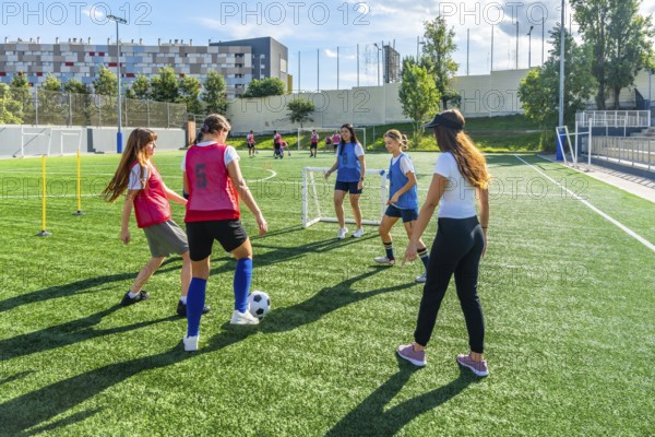 Female soccer teammates training on a sunny artificial turf field, practicing dribbling, passing