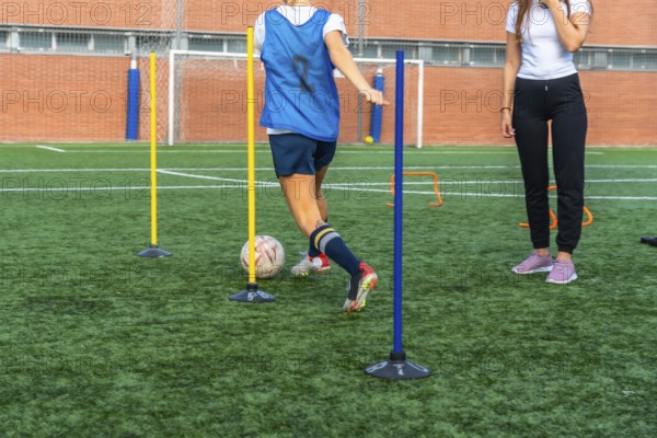 Young woman in a blue bib practicing soccer dribbling skills, maneuvering a ball through training
