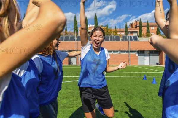 Young women's soccer team celebrating a goal, arms raised and cheering with bright smiles on a