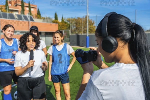 Videographer with headphones filming a reporter holding a microphone and interviewing a group of