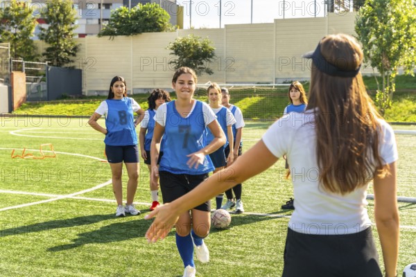 Young women's soccer team participating in a training session on a sunny artificial turf field,