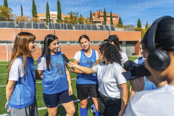 Women soccer team players standing on a green sports field, one player holding a microphone while