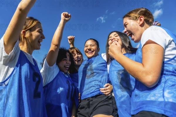 Diverse group of young women soccer players celebrating a goal or victory, raising fists and