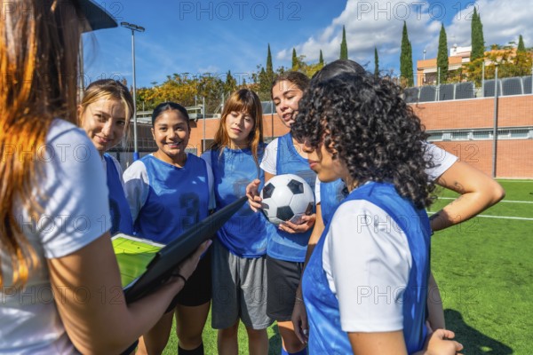 Women's soccer team huddling with their coach on a green artificial turf field, listening intently
