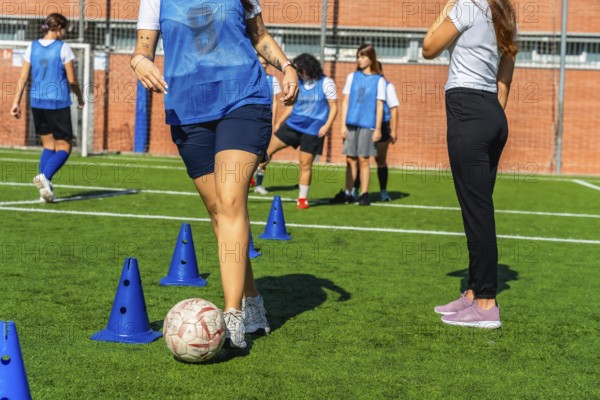 Young women's soccer team practicing dribbling drills with cones on green turf, focused and