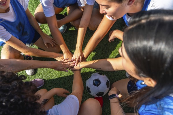 Women soccer players huddling on the green field, joining hands in a sign of unity and strength