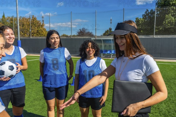 Coach, wearing a visor and holding a folder, explaining strategy to a smiling female soccer team on