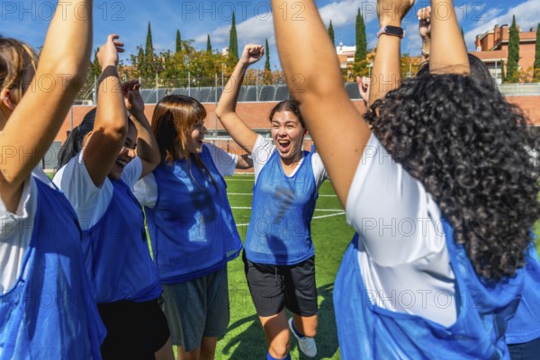 Women soccer players raise their arms and cheer in victory on a sunny outdoor field, celebrating