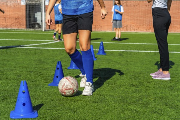 Young girl in a blue jersey practicing soccer dribbling skills around orange cones on a green