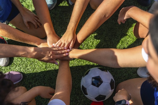 United women soccer players stacking hands in a huddle on the green artificial grass field, showing