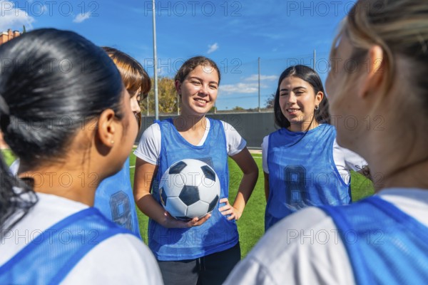 Women soccer players in blue uniforms huddled on a green field, smiling and planning strategy