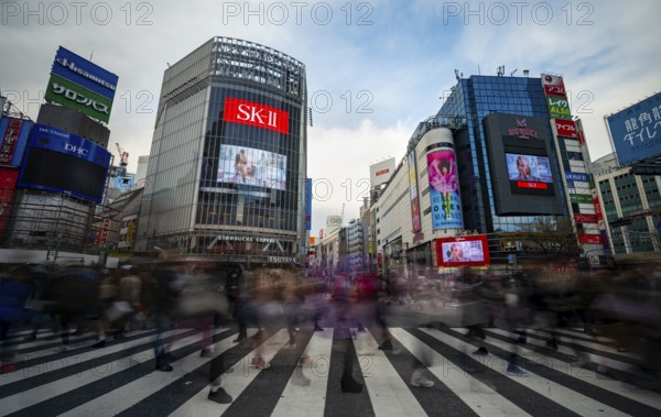 Crowd crossing zebra crossings on a large intersection, motion blur, modern houses with colorful