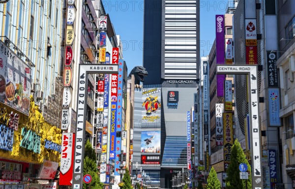Bustling street scene in Japan with modern buildings and colorful billboards, figure of Godzilla