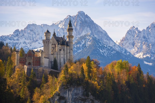 Neuschwanstein Castle is enthroned against an impressive mountain backdrop, surrounded by autumnal