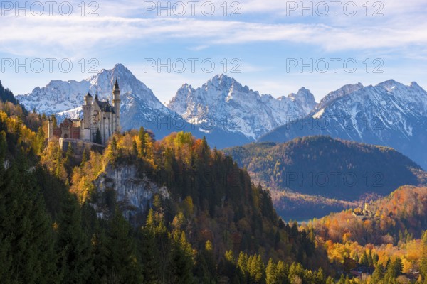 The majestic Neuschwanstein Castle on a mountain with autumn-colored forest in the foreground,