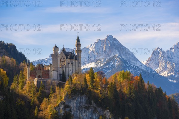 Neuschwanstein Castle rises impressively against a snowy mountain backdrop, surrounded by autumnal