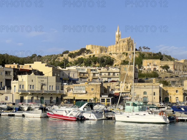 View of front sports boats sailboat in Mgarr harbour behind houses, on hills in the background