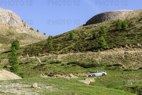 Porsche GT3 sports car drives on mountain road above tree line Col de d' Izoard l' Izoard l'Izoard