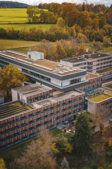 Modern architecture with surrounding forests and meadows in autumn colors, solar cells visible,