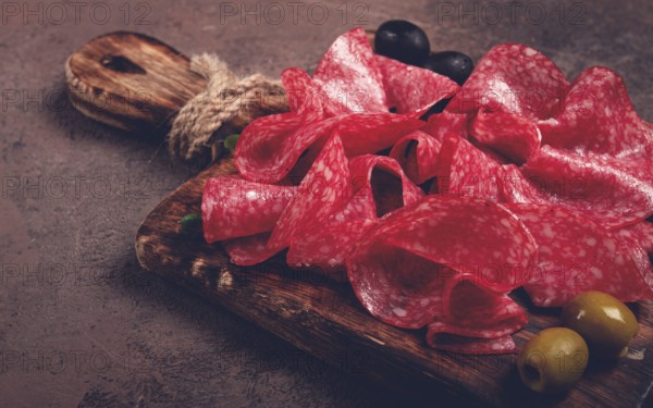 Sliced salami sausage, on a wooden chopping board, decorated with olives and herbs, close-up, no