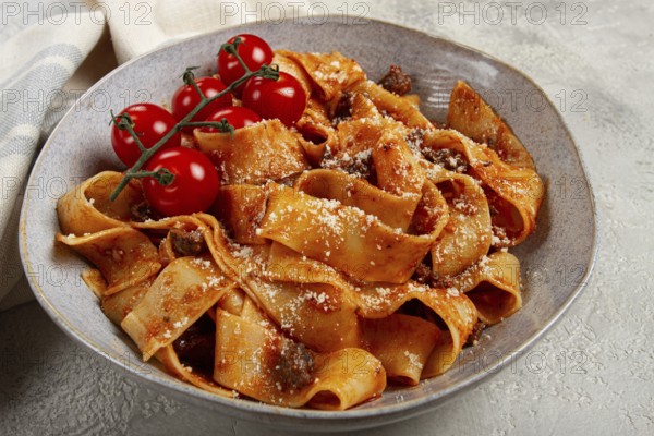 Pappardelle pasta with bolognese sauce, topped with parmesan cheese and cherry branch, homemade, no