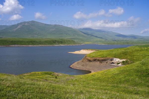 A calm lake surrounded by green hills and mountains under a blue sky with clouds, Spandaryan